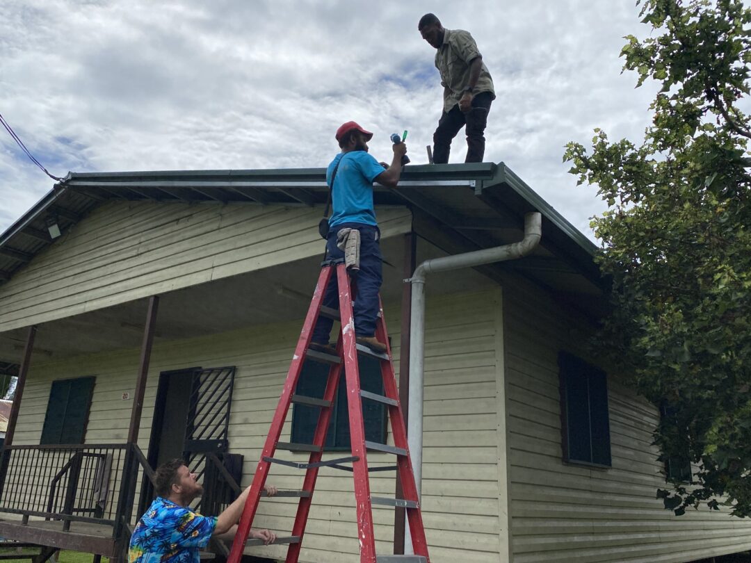 ExpandingInternetAccess Employees along with a New Zealand volunteer use a ladder to get on the roof of a yellow house to set up better internet hardware